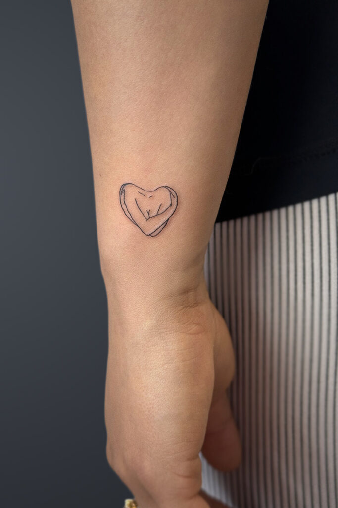 Aesthetic Tattoo Art| Fine line tattoo of the torso of aa woman, holding her arms, in the shape of a heart